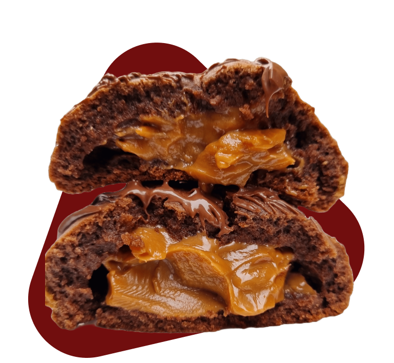 
A imagem mostra um cookie de chocolate cortado ao meio pulsante, revelando um recheio cremoso e dourado, que se assemelha a doce de leite. O doce tem uma casca externa de chocolate escuro e parece ter uma textura macia, quase como um bolo ou biscoito denso. Há também um pouco de calda de chocolate escorrendo sobre o recheio e a casca, sugerindo um acabamento ainda mais indulgente. A peça está dividida horizontalmente, exibindo claramente as duas metades com o recheio abundante. O fundo da imagem é predominantemente claro, com uma forma orgânica de cor bordô ou marrom escura atrás do doce, que realça o objeto principal.